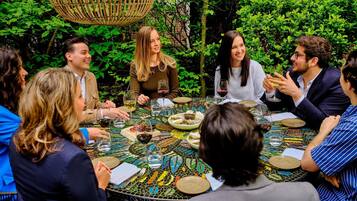 A group of people seated around a round table with a mosaic tablecloth, engaged in conversation.