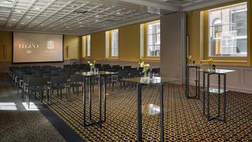 Une salle de conférence dotée d’un tapis à motifs, d’un grand écran affichant le logo de Sofitel Legend, et de plusieurs tables entourées de chaises.
