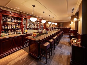 A bar area with a long counter, multiple stools, and a variety of bottles on shelves.
