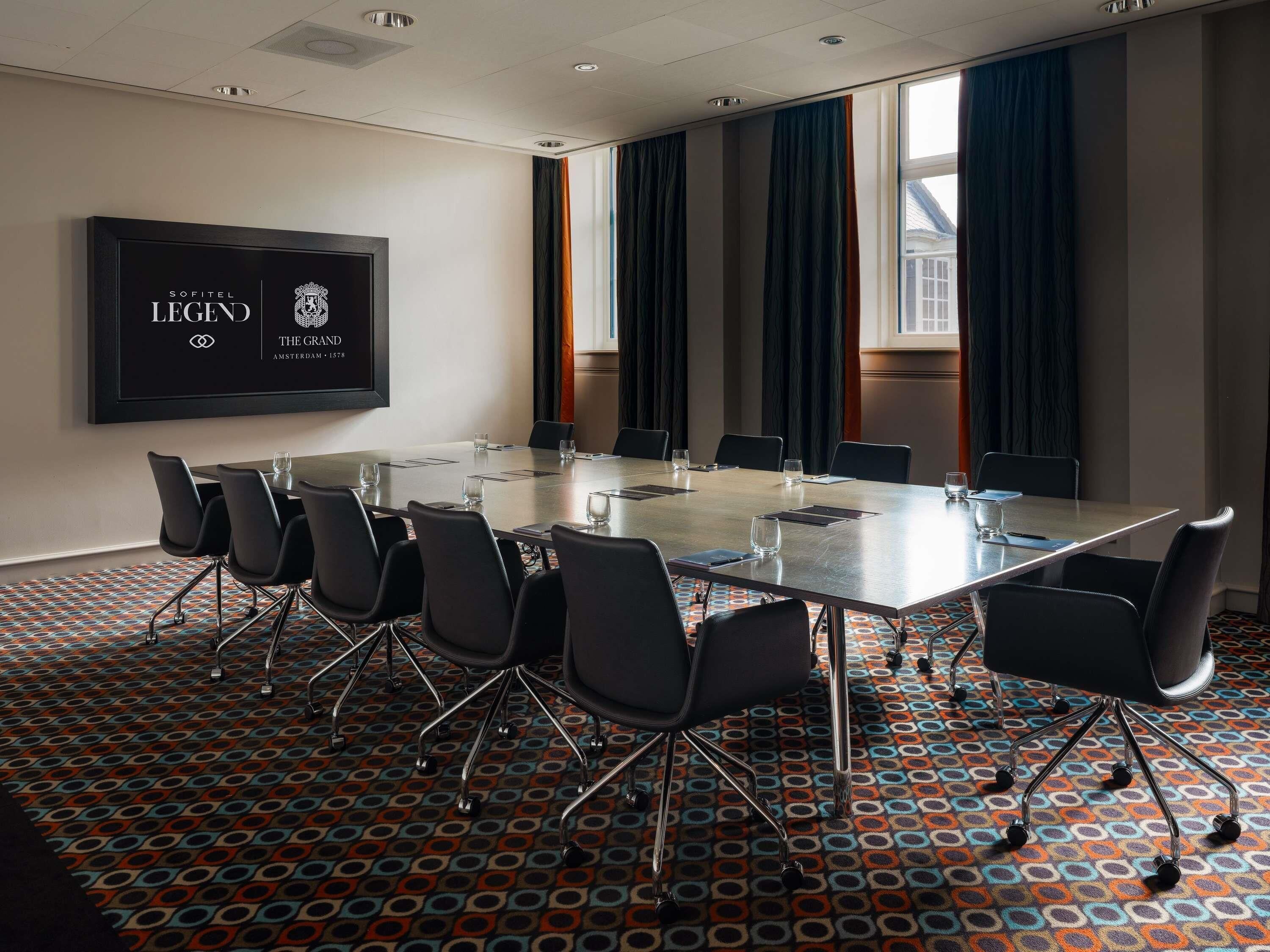 Un salón de conferencias con una larga mesa, sillas, una pantalla y alfombra estampada.