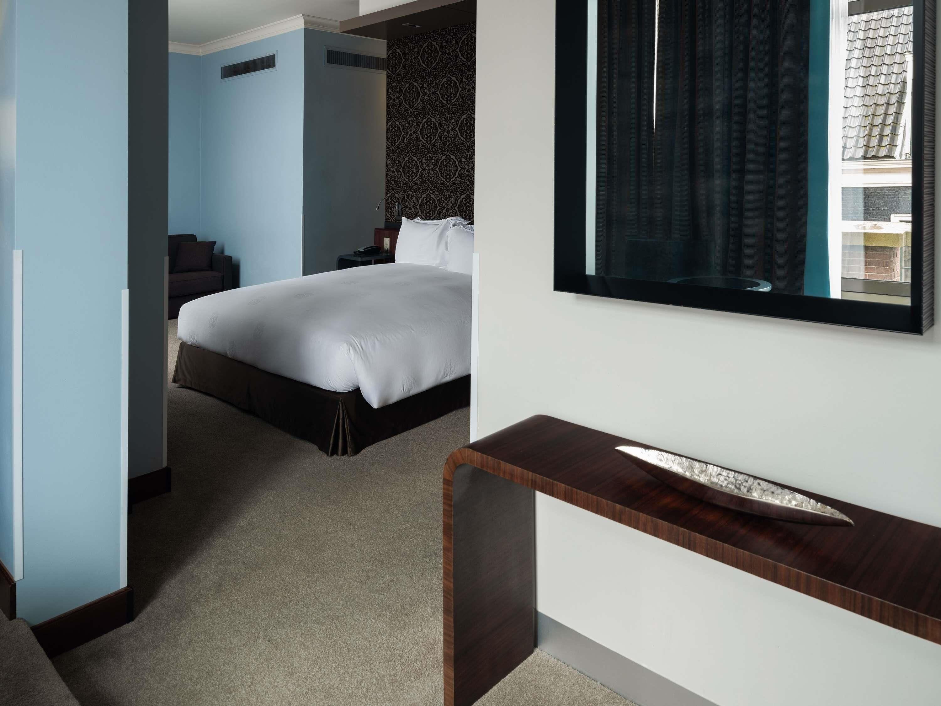 A hotel room with a bed, a desk, and a large mirror.