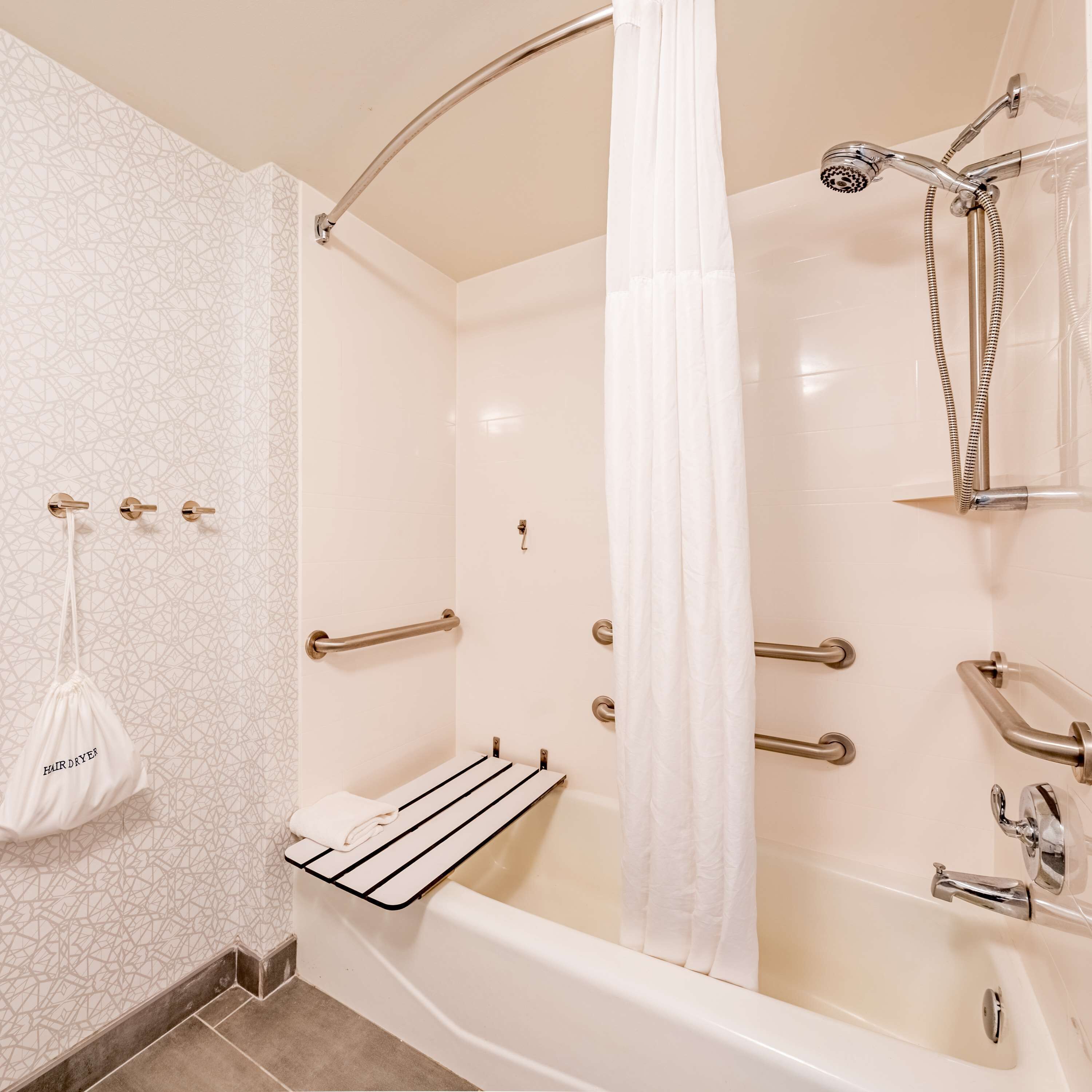 A modern bathroom with a walk-in shower, grab bars, a towel rack, and a hairdryer.