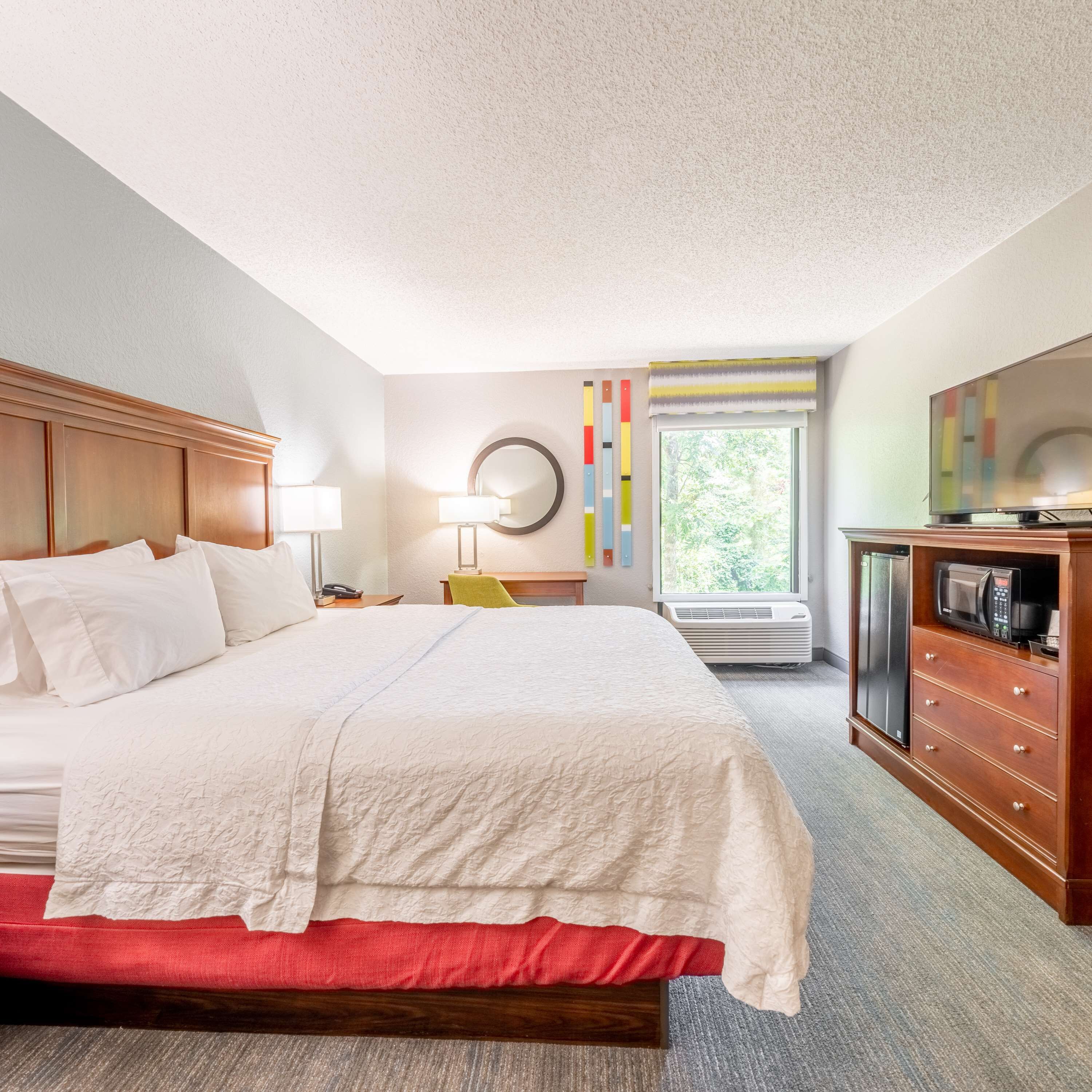 A hotel room with a large bed, a desk with a chair, a television, and a minibar.