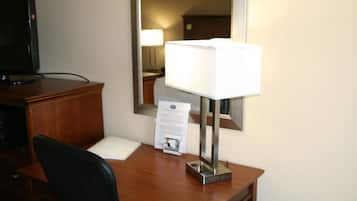 Habitación de hotel con escritorio de madera, lámpara, televisor y espejo.