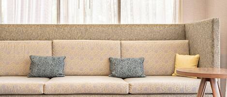 A modern living room with a beige sofa, two patterned cushions, a small round wooden table, and two red chairs.