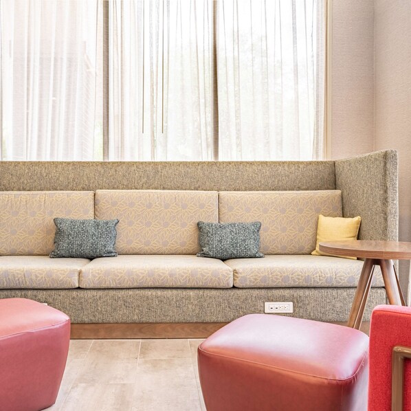 A modern living room with a beige sofa, two patterned cushions, a small round wooden table, and two red chairs.