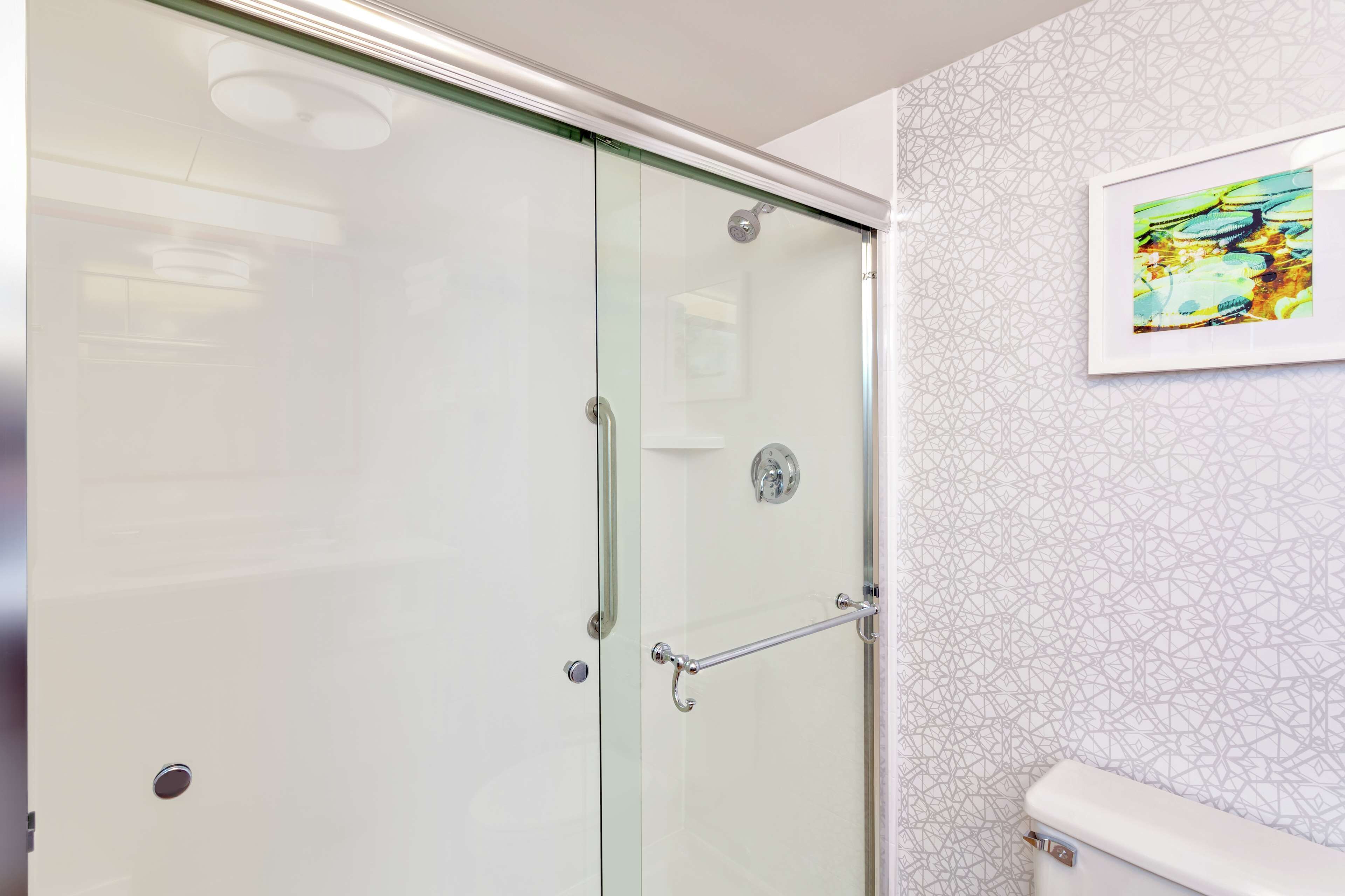Une salle de bain moderne avec une douche à parois de verre, des toilettes blanches et un mur décoré d’un motif.