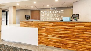 Un mostrador de recepción de hotel con paneles de madera, un quiosco digital y un cartel que dice 'Welcome to the Sun Shine State'.