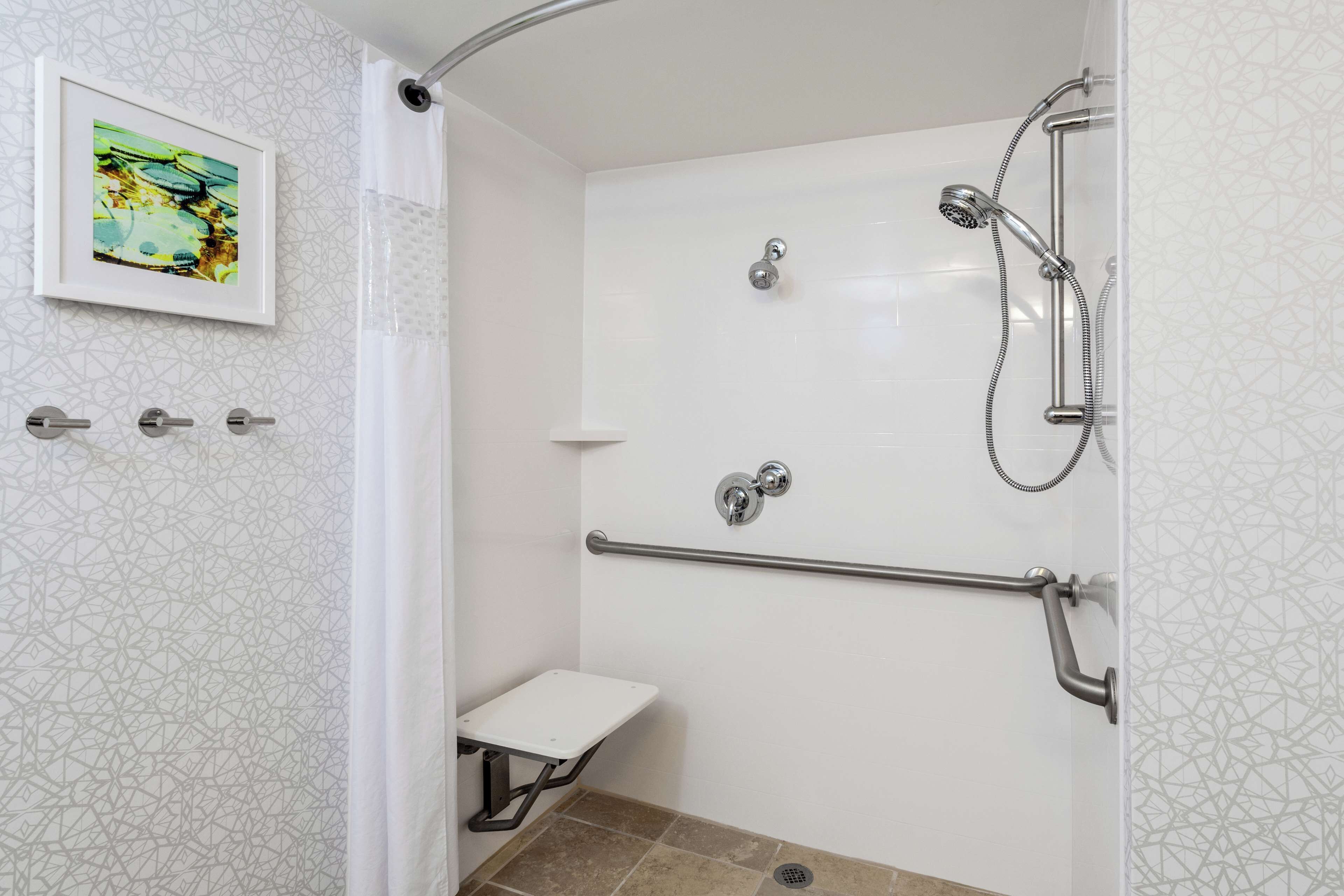 A shower with a handrail, a small bench, and a picture on the wall.