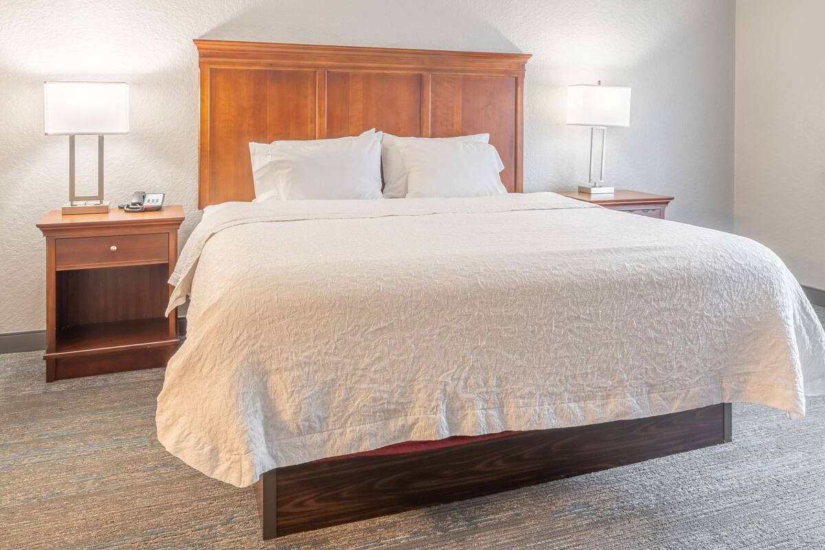 A neatly made bed with a wooden headboard, two bedside tables with lamps, and a carpeted floor.