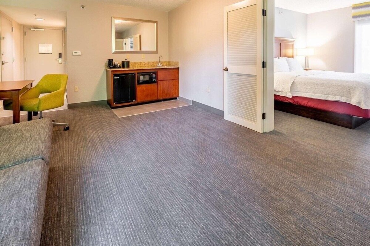 A hotel room with a bed, a desk, a chair, a dresser, and a mirror.