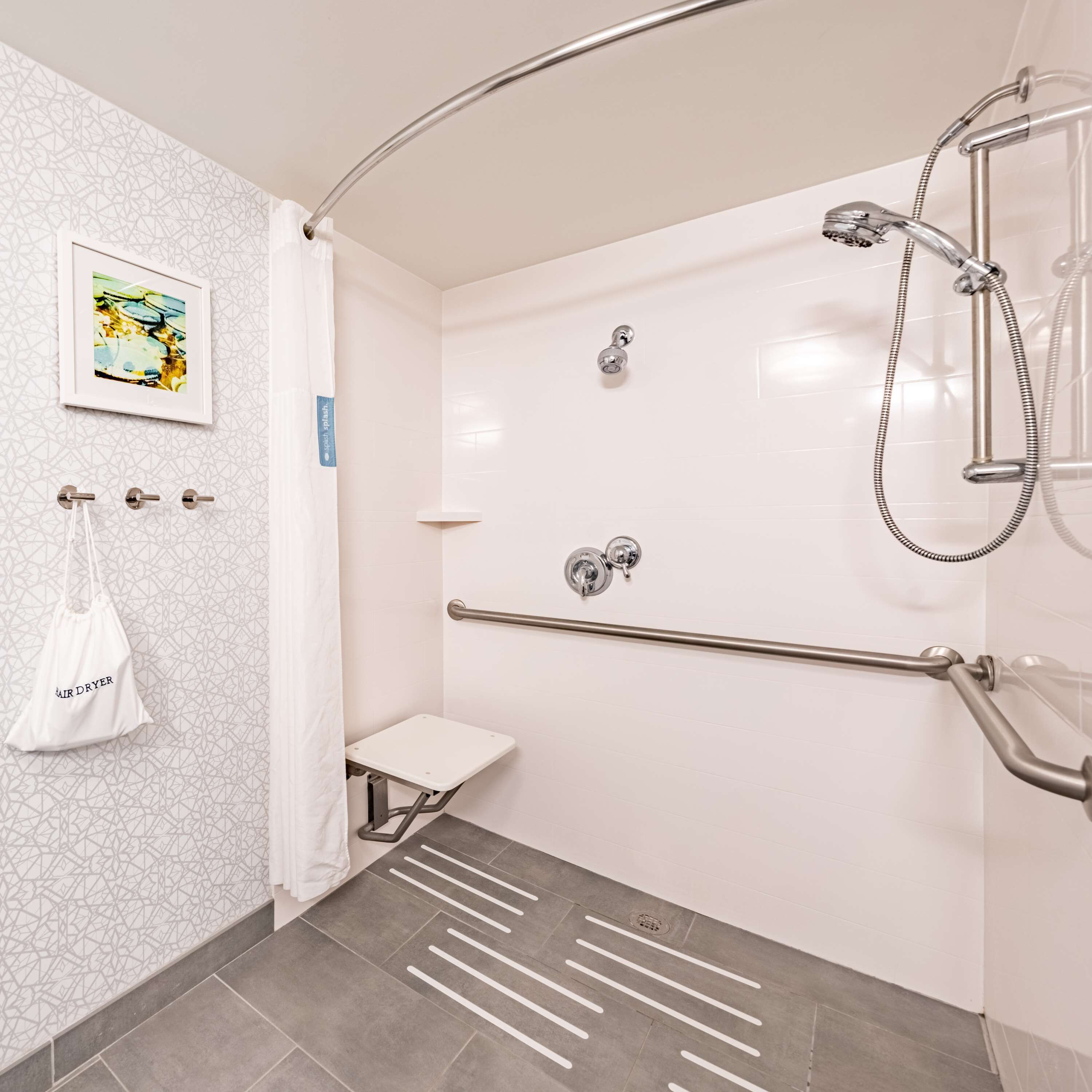 Ein modernes Badezimmer mit Dusche, Haltegriffen, einer kleinen Toilette und einem Handtuchhalter.