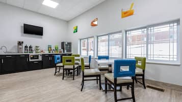 A modern kitchen with a flat-screen TV, coffee machines, and a large window with a view of the outside.