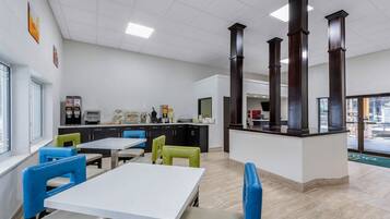 A modern dining area with tables and chairs, a kitchen area, and a counter with a view.