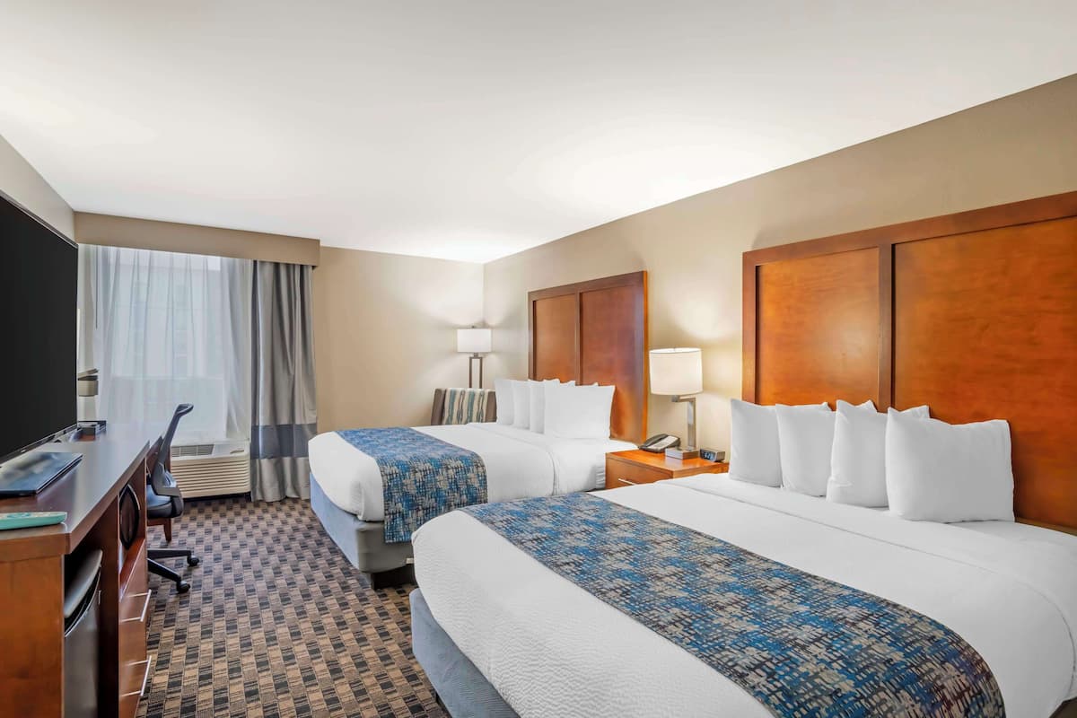 Une chambre d’hôtel avec deux lits, un bureau, une télévision et une fenêtre avec des rideaux.