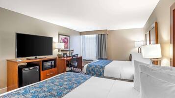 Habitación de hotel con dos camas, un escritorio, televisor, refrigerador pequeño y ventana con cortinas.