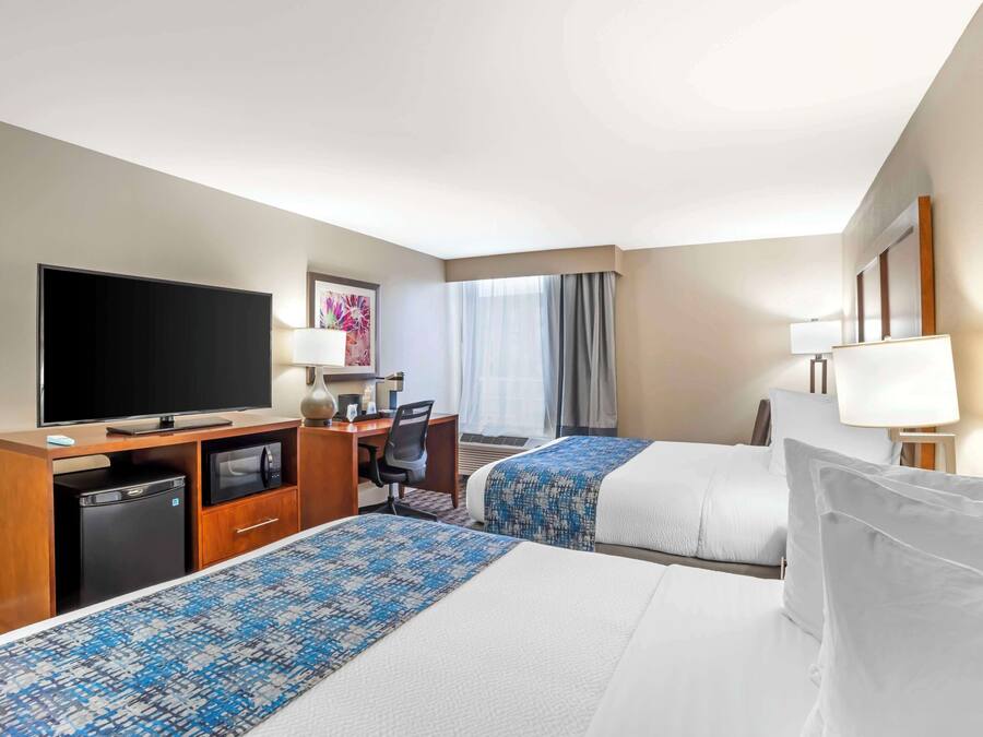 Habitación de hotel con dos camas, un escritorio, televisor, refrigerador pequeño y ventana con cortinas.