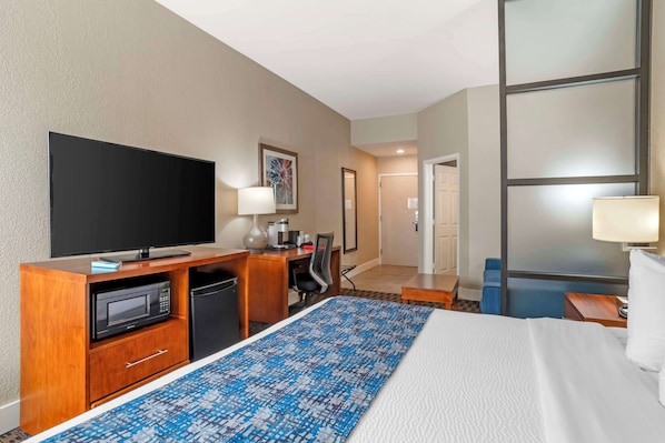 Una habitación de hotel con cama, escritorio, televisor, microondas y cafetera.