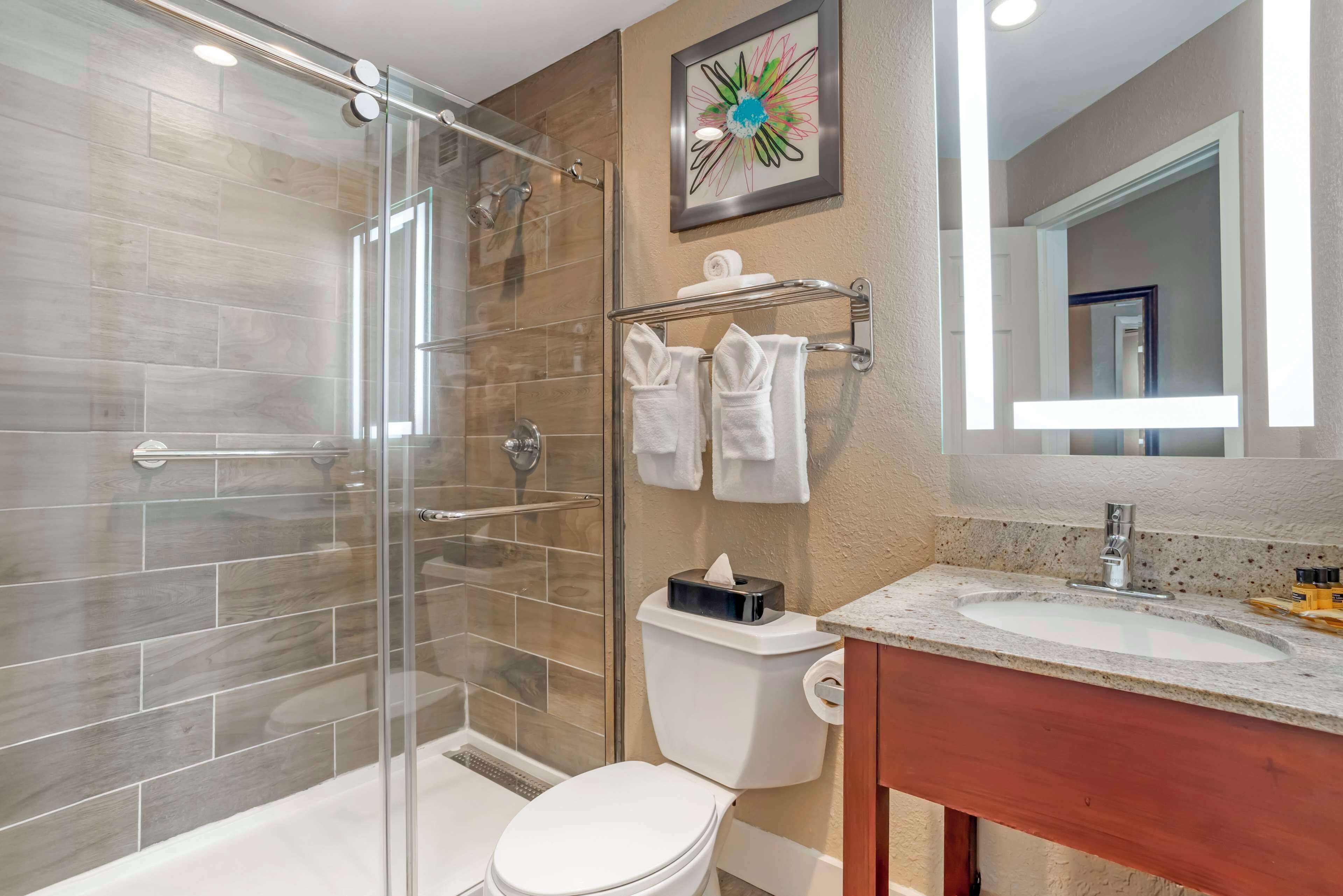 A modern bathroom with a glass-enclosed shower, a toilet, a sink with a marble countertop, and a mirror.