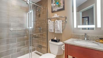 A modern bathroom with a glass-enclosed shower, a toilet, a sink with a marble countertop, and a mirror.