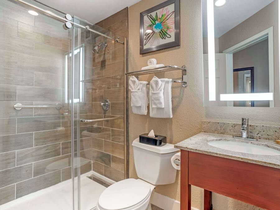 A modern bathroom with a glass-enclosed shower, a toilet, a sink with a marble countertop, and a mirror.