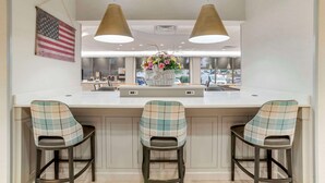 Una cocina moderna con una isla central, tres taburetes de bar, iluminación colgante y un arreglo floral decorativo.