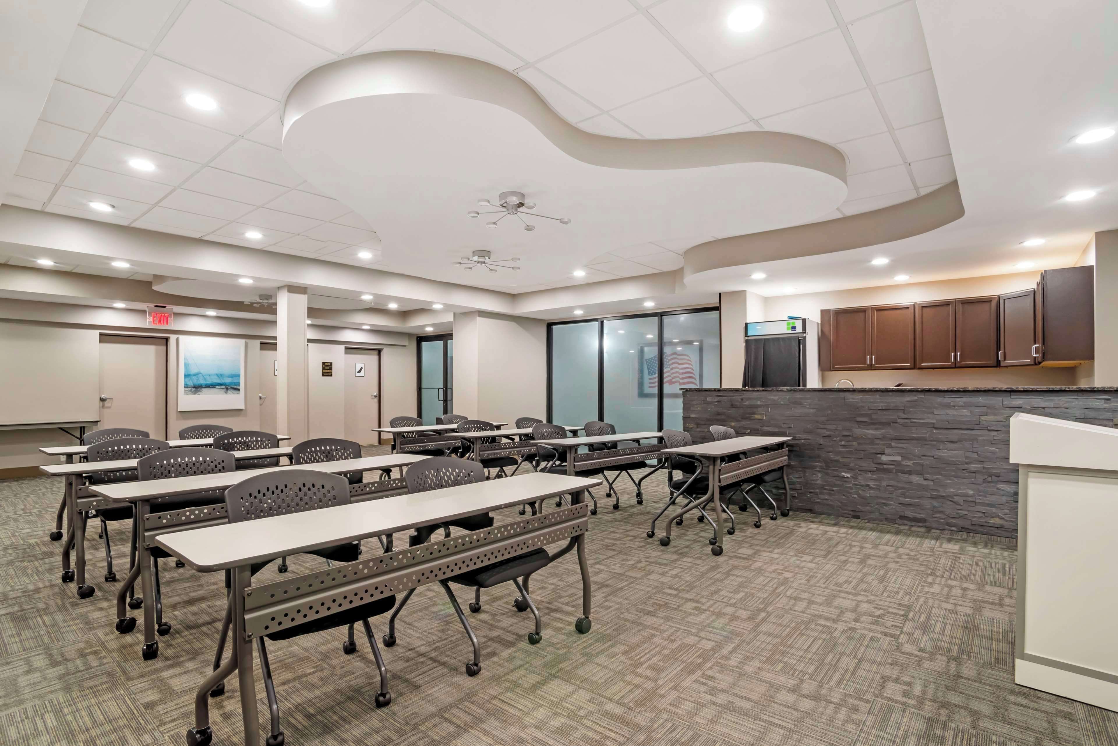 Une salle de conférence équipée de tables et de chaises, d’un tableau blanc et d’un mur décoratif en pierre.