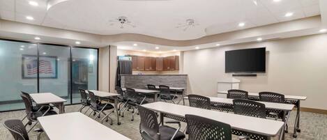 A conference room with tables and chairs, a projector screen, and a television on the wall.