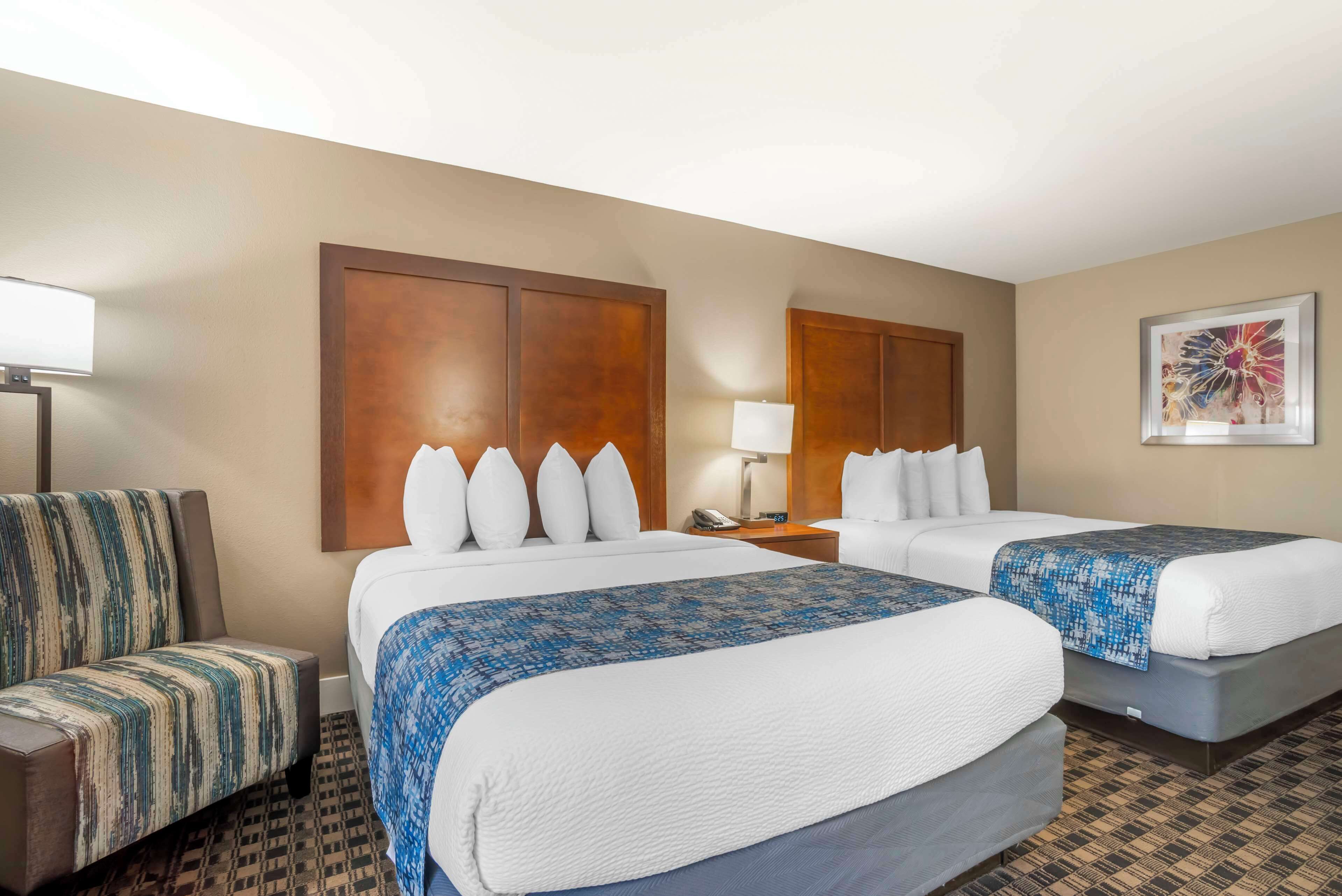 A hotel room with two beds, a sofa, a nightstand with a lamp, and a wall-mounted artwork.