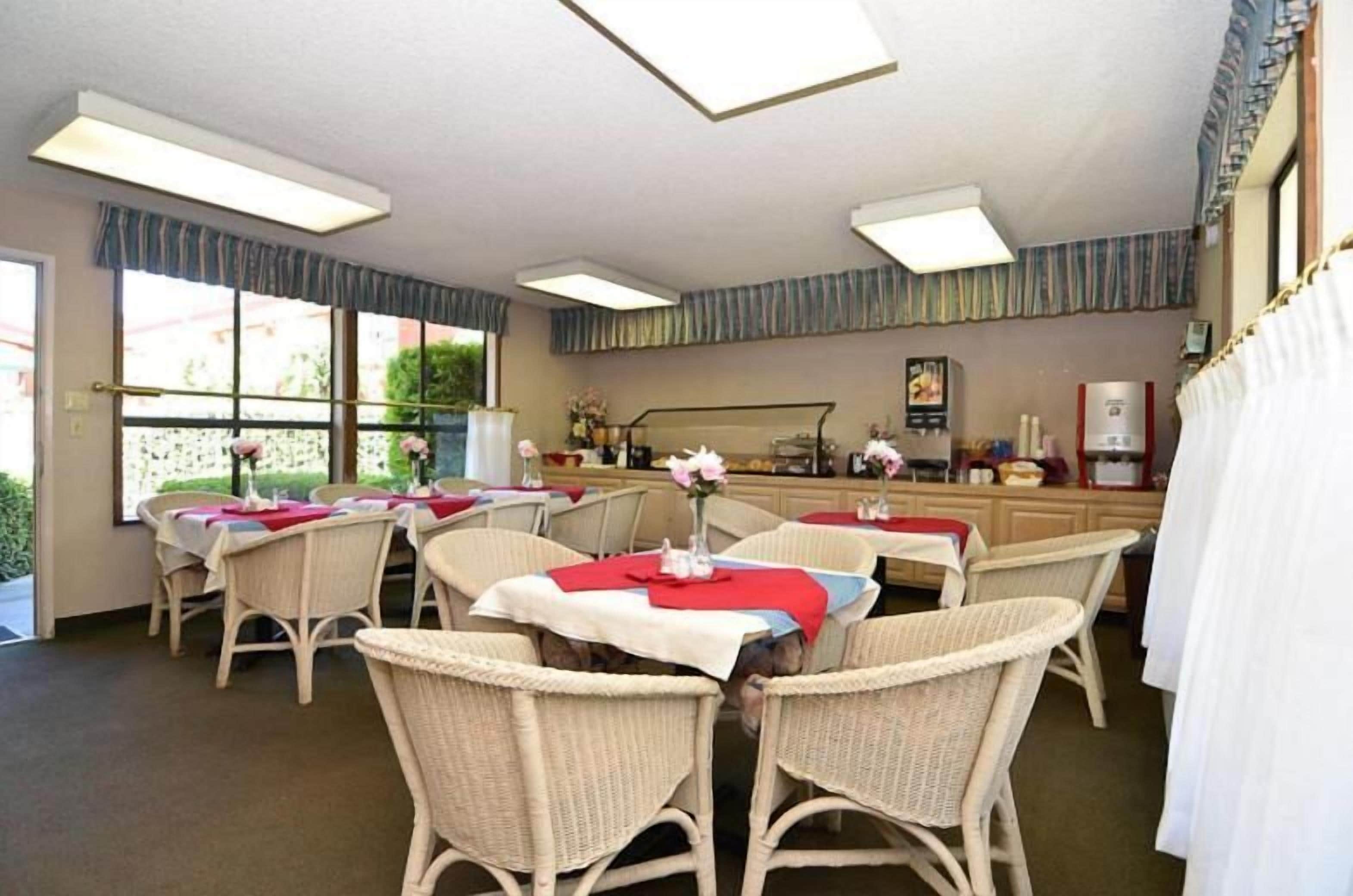 Un coin repas avec des chaises et des tables en osier, un espace cuisine équipé d’une machine à café, et une fenêtre donnant sur un paysage verdoyant.