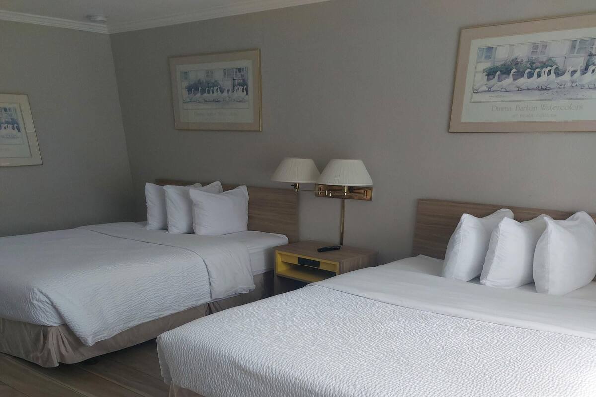 A hotel room with two beds, a nightstand with lamps, and framed artwork on the walls.