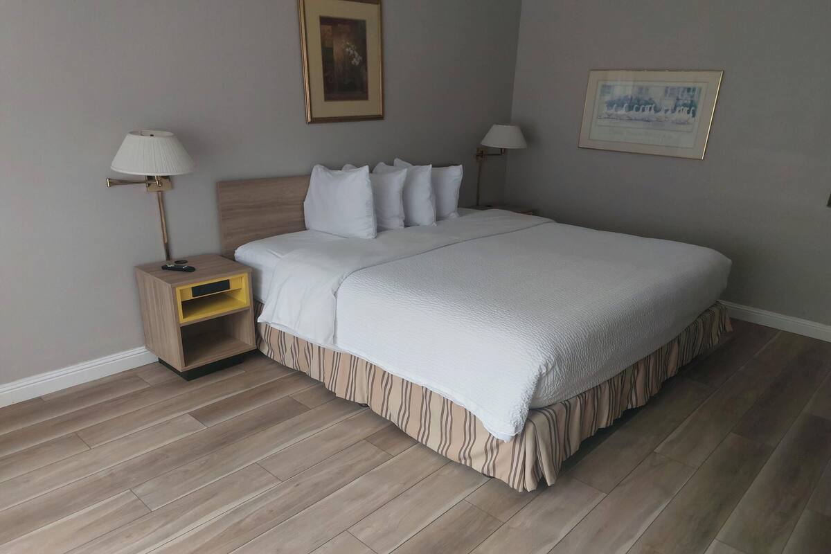 A neatly made bed with white bedding, a wooden nightstand with a lamp, and a framed picture on the wall.