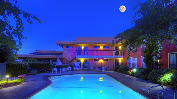 A hotel with a swimming pool, outdoor seating, and a moon in the sky.