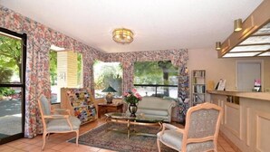 A cozy living room with floral wallpaper, a glass coffee table, and two armchairs.