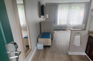 Un baño con un banco de madera, un cubo de basura, un perchero para toallas y un espejo.