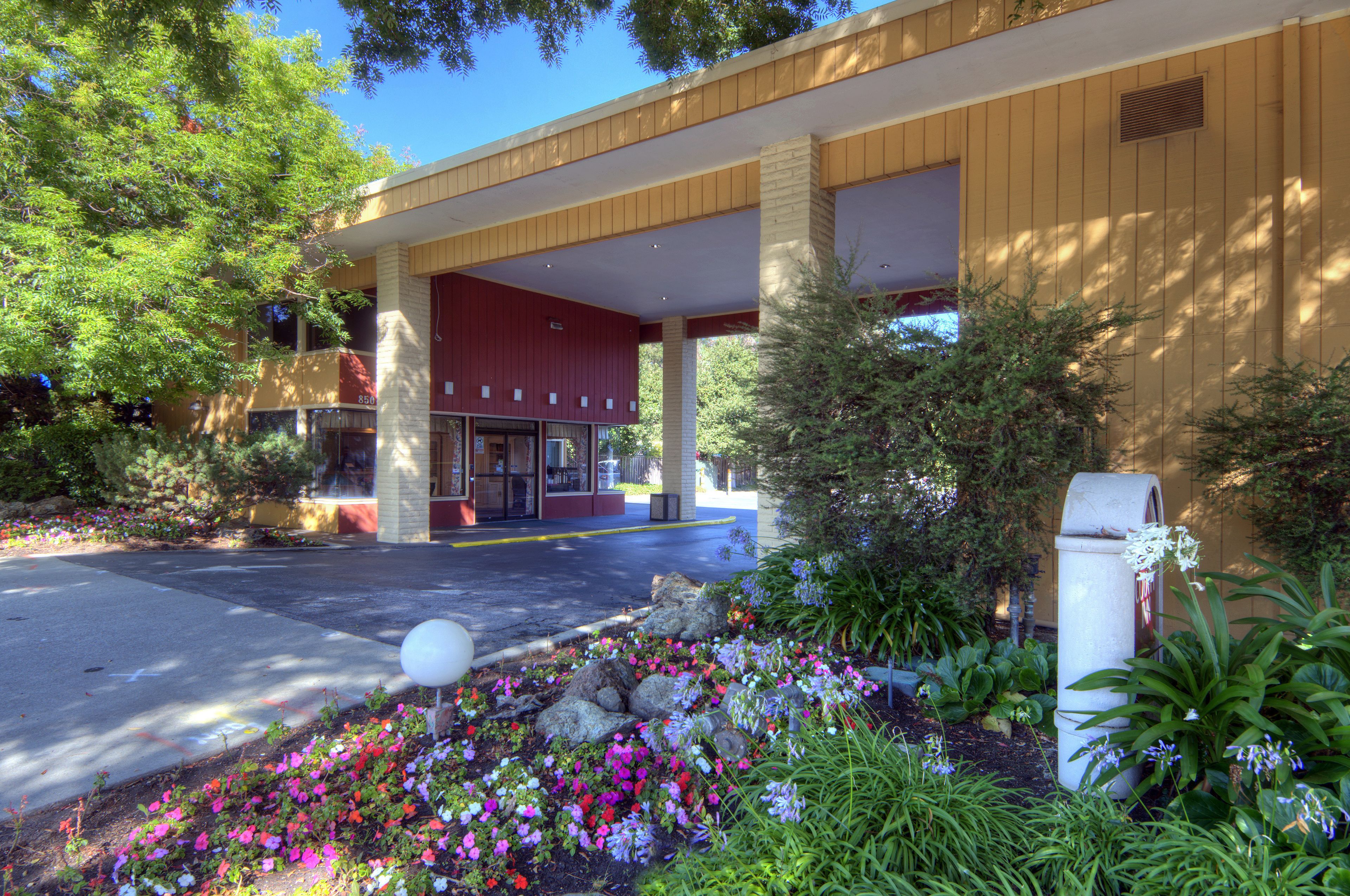 A building with a covered entrance, a flower garden in front, and a mailbox.