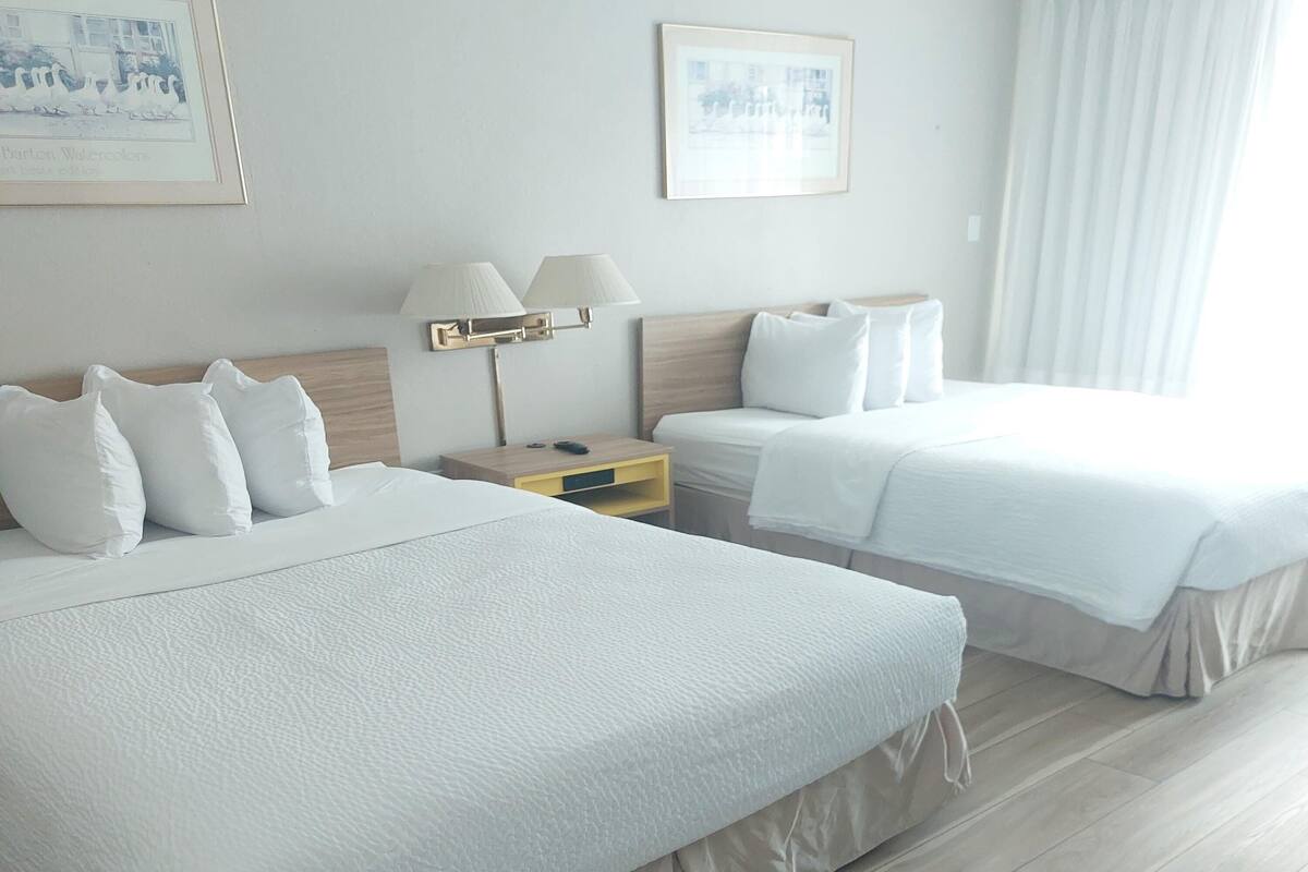 A hotel room with two beds, a nightstand with lamps, and framed pictures on the walls.