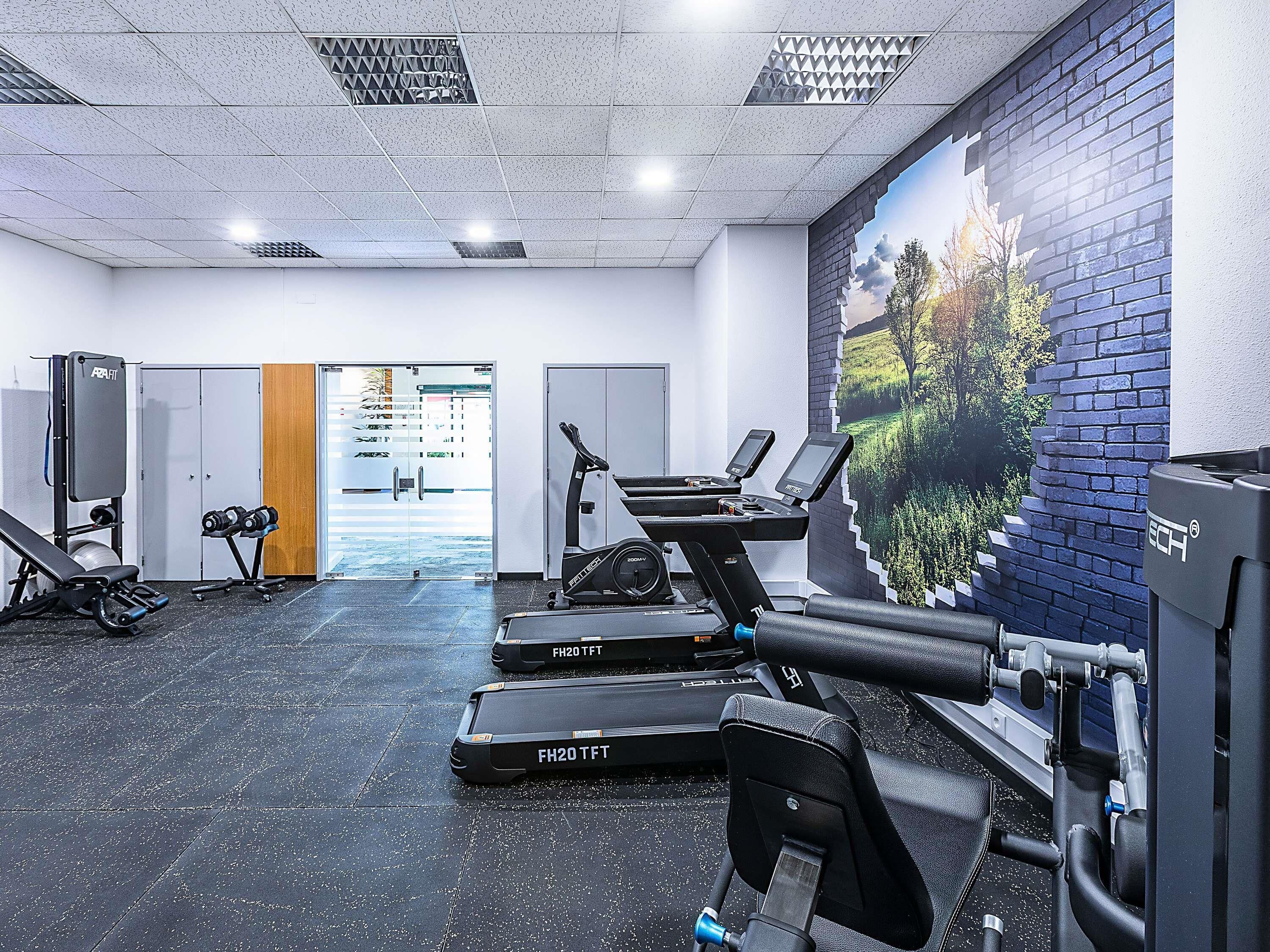 A gym with treadmills, weight machines, and a mural on the wall.