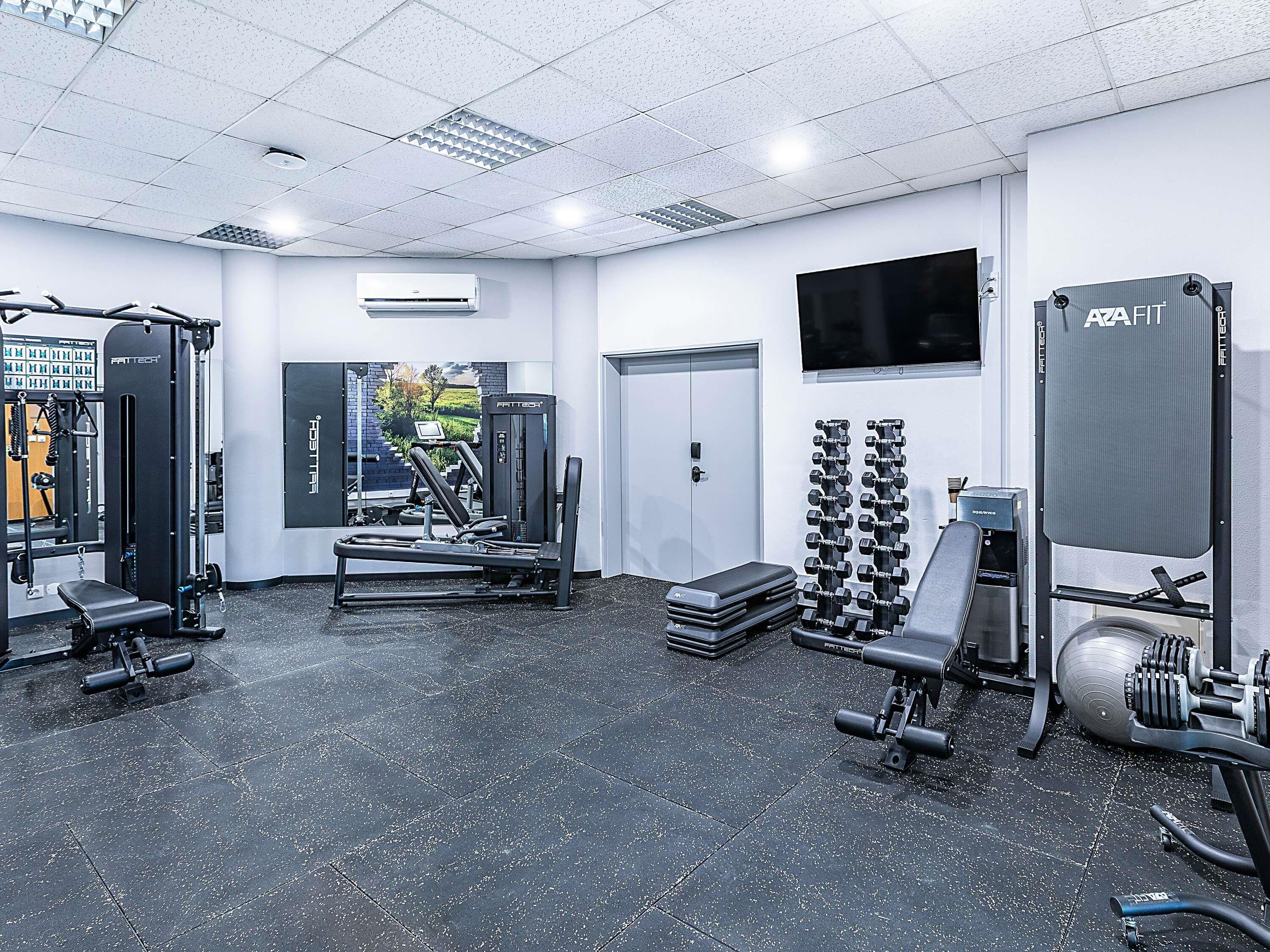 A gym with various exercise equipment, a wall-mounted TV, and a door leading to another room.