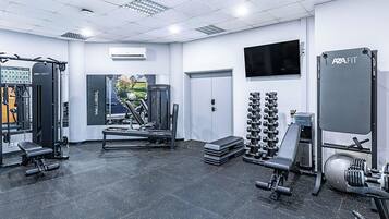 A gym with various exercise equipment, a wall-mounted TV, and a door leading to another room.