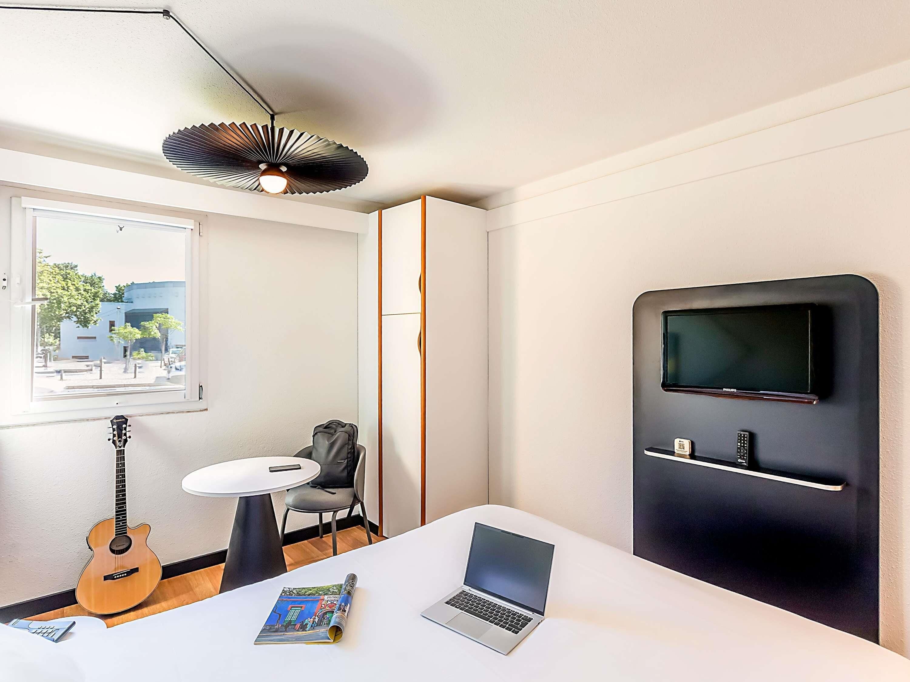 A modern room with a laptop, a guitar, a magazine, a TV, and a chair.