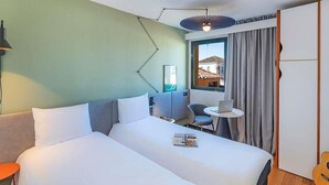 A hotel room with a bed, a desk, a chair, a laptop, and a view of buildings outside the window. - ibis Evora Hotel (Évora)