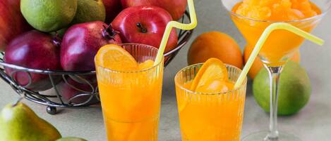 Un frutero con manzanas y naranjas, y dos vasos de zumo de naranja con pajitas.