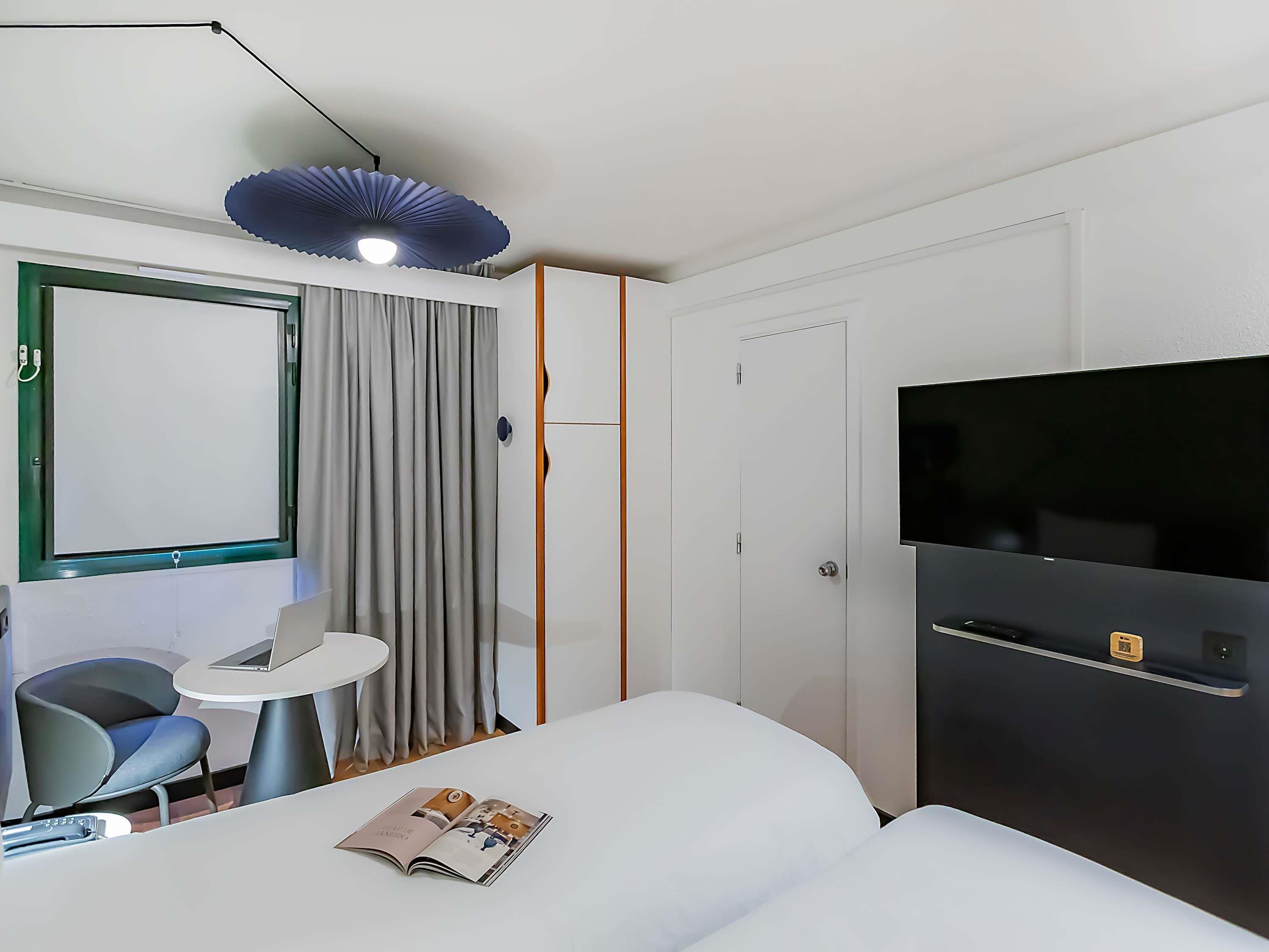 Una habitación de hotel moderna con una cama, televisión, una mesita y una silla.