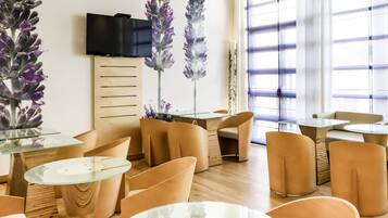 A modern interior with round tables and chairs, a flat-screen TV, and large windows.