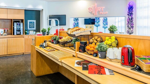 A breakfast bar with various food items, a coffee machine, and a sign that reads "START ME UP". - ibis Evora Hotel (Évora)