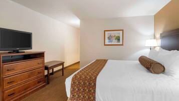 A hotel room with a bed, a television on a wooden dresser, a bench, and a framed picture on the wall.