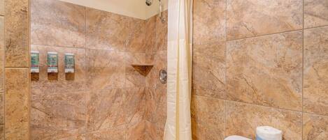 A bathroom with a shower, a toilet, and a shelf with toiletries.