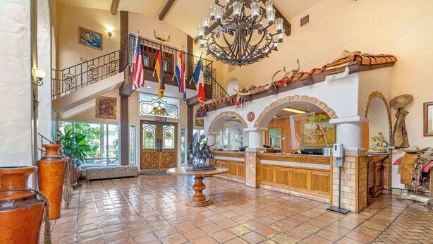 A lobby with a grand staircase, a chandelier, and a reception desk. - Best Western Casa Grande Inn (Pismo Beach)
