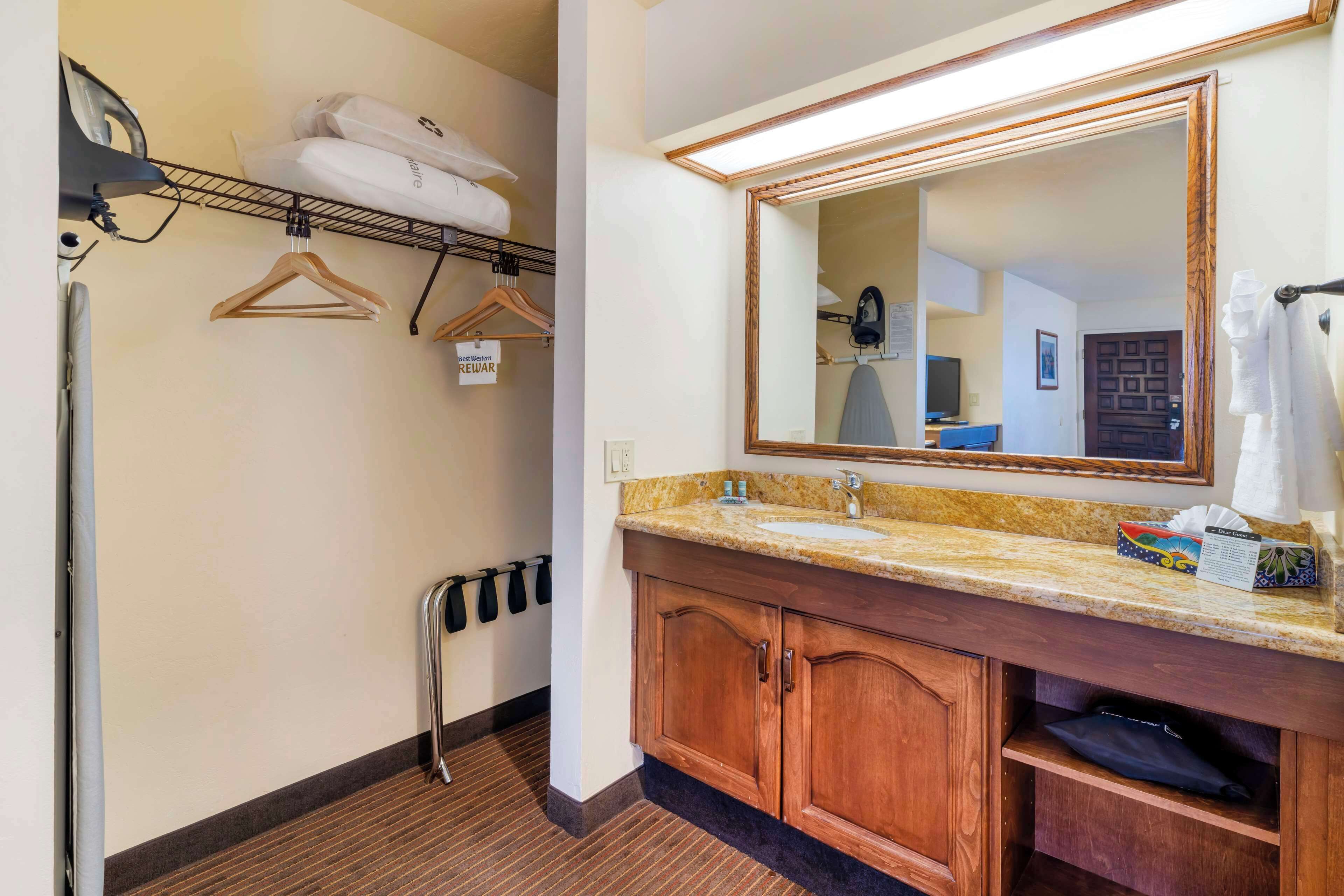 A hotel bathroom with a granite countertop sink, wooden cabinets, a large mirror, and a towel rack.